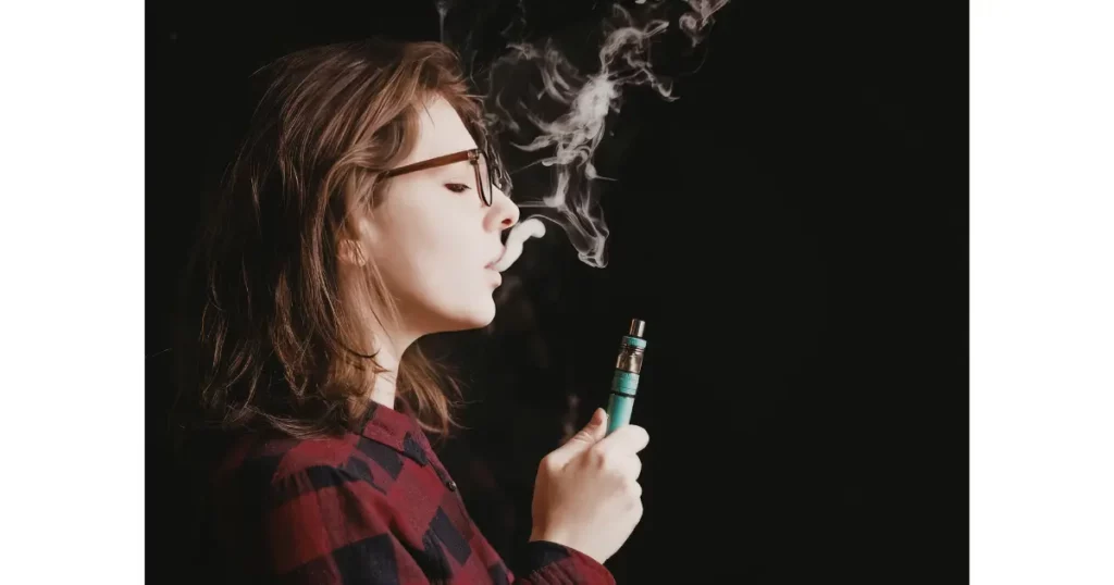 Młoda kobieta wypuszcza chmurę aerozolu z e-papierosa — wapowanie a ryzyko raka płuc u młodych dorosłych.